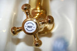 A close-up view of a gold faucet featuring a sign attached to it, highlighting its elegant design and functionality.