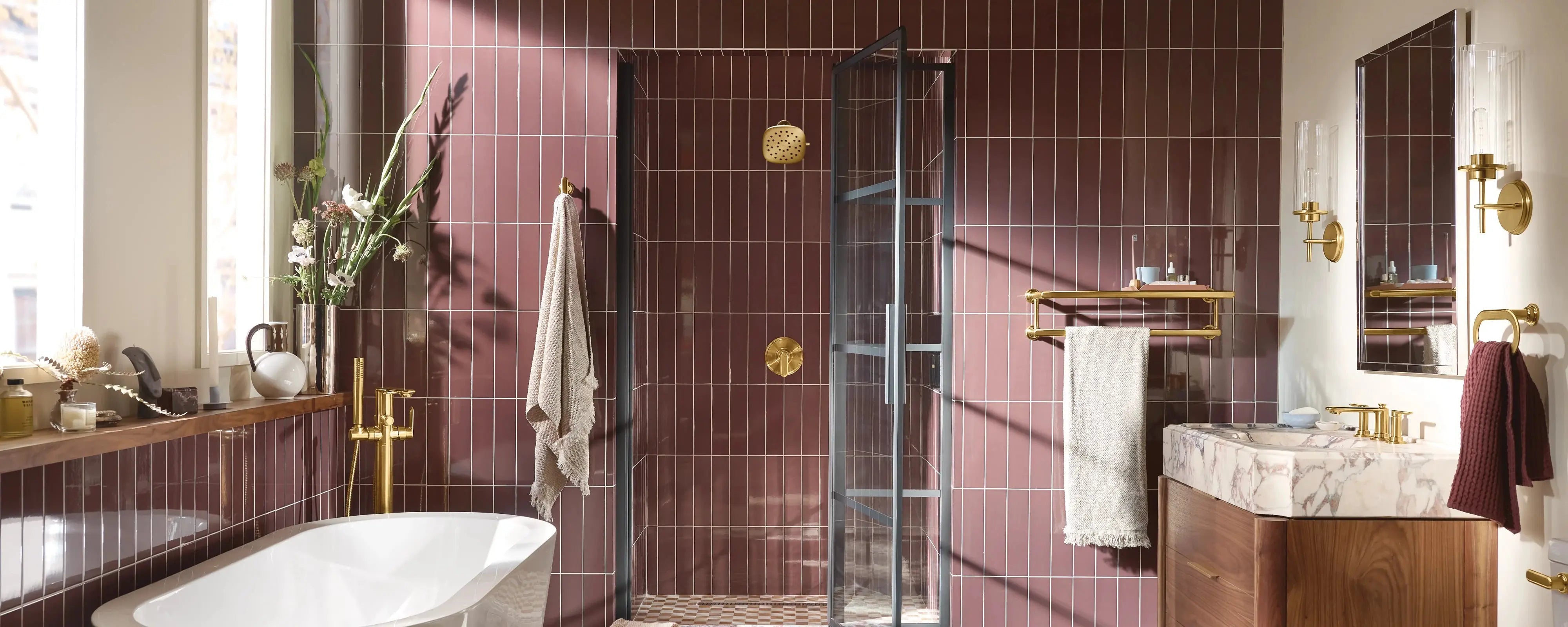 Modern bathroom with gold Moen Faucets, featuring a freestanding bathtub, maroon wall tiles, glass shower door, and elegant vanity with marble countertop. (Moen Faucets)